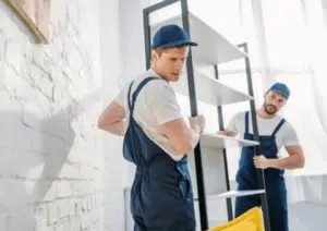 Due ragazzi con delle tute da lavoro blu che spostano uno scaffale di ferro